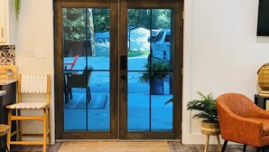 Ein Zimmer mit Holzboden, einem gewebten Teppich, einem hölzernen Stuhl, einem gepolsterten Sessel, einem kleinen Tisch und einer Topfpflanze.