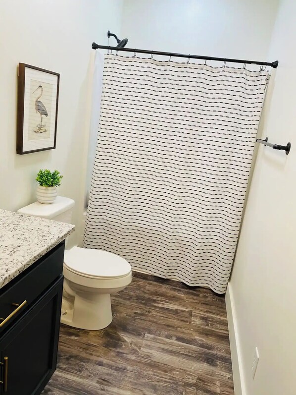Un baño con inodoro, lavamanos, un cuadro enmarcado y cortina de ducha.