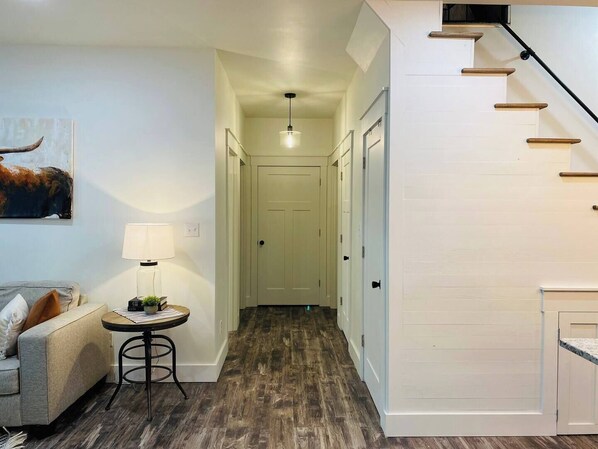 A hallway with a staircase, a lamp, a table with a plant, and a painting of a bull. - Cooter Valley on The Rough (Falls of Rough)