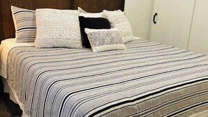 Ein ordentlich bezogenes Bett mit Streifenmuster, ein hölzernes Kopfende und ein dekorativer Spiegel an der Wand.