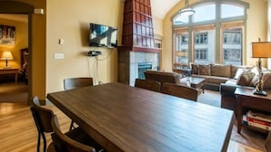 A spacious living area with a wooden dining table, a fireplace, and a large window providing natural light. - 4 bdr Swiss chalet in Solitude, 5 min to lifts (Salt Lake City)