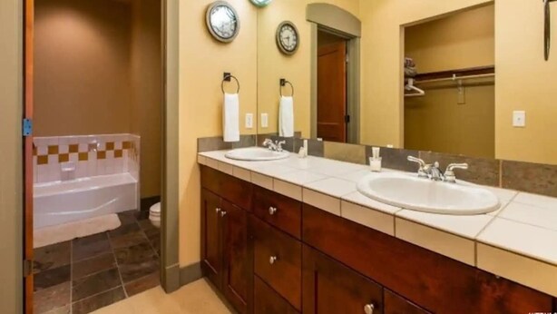 Un baño con lavamanos doble, bañera y un espejo grande.