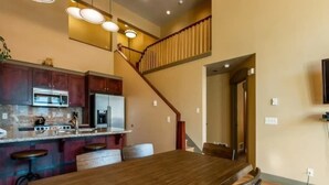 A modern kitchen with a wooden dining table and bar stools, a staircase, and a view of the living area. - 4 bdr Swiss chalet in Solitude, 5 min to lifts (Salt Lake City)