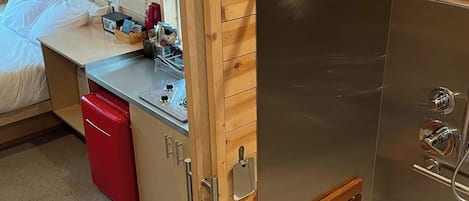 Una habitación compacta con cama, una kitchenette pequeña, un electrodoméstico rojo y zona de ducha.