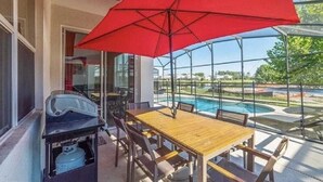 Eine Terrasse im Freien mit einem Holztisch, Stühlen, einem roten Sonnenschirm und einem Grill.