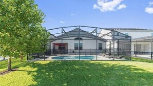 Ein überdachter Pool im Freien mit Metallrahmen und Glasscheiben, umgeben von einem gepflegten Rasen und einem Baum.