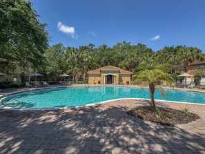 A swimming pool with a curved edge, surrounded by a paved walkway and shaded by trees. - Spacious Lakefront Townhouse | 10 Mins to Disney & Resort Pool Access (Kissimmee)