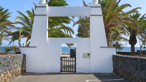 A white gate with a view of the sea, surrounded by palm trees.