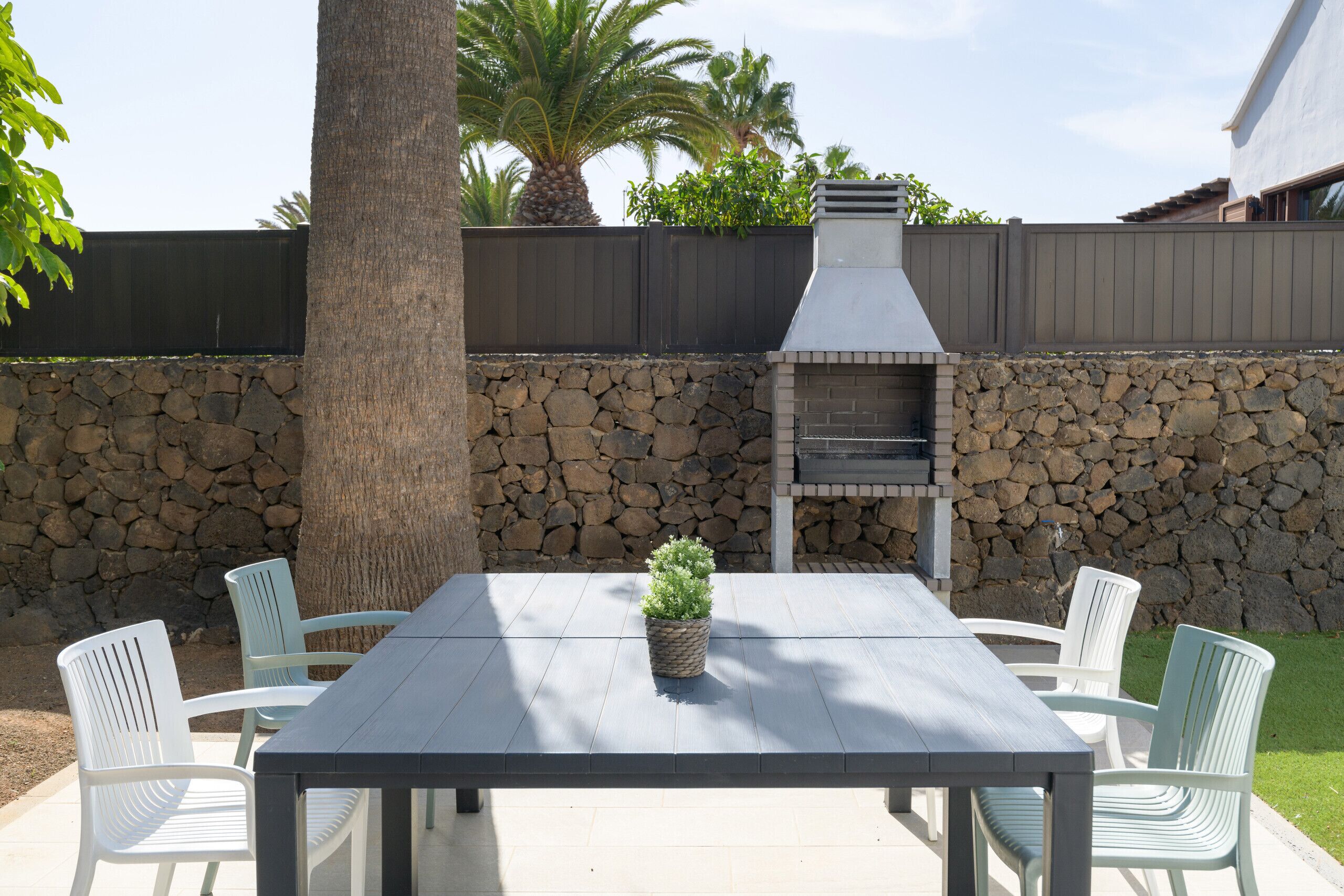 An outdoor patio with a stone wall, a wooden table, and four white chairs.