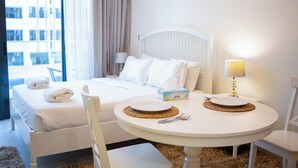 A hotel room with a bed, a round dining table with chairs, a lamp, and a window with curtains.