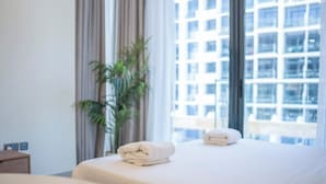 A hotel room with two beds, a potted plant, and a view of a building through large windows.