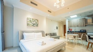A modern hotel room with a large bed, a small sofa, a dining table with chairs, a kitchenette, and a ceiling light. - AWS Holiday Homes - In the Heart of Downtown (Dubai)
