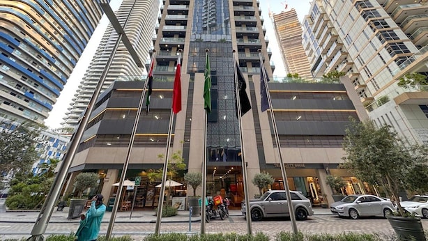 A modern building with multiple floors, a prominent entrance, and flags. - AWS Holiday Homes - In the Heart of Downtown (Dubai)