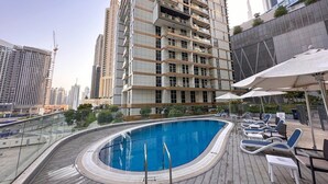 A rooftop swimming pool with lounge chairs and umbrellas, surrounded by high-rise buildings. - AWS Holiday Homes - In the Heart of Downtown (Dubai)