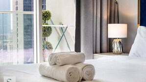 Hotellihuone, jossa on sänky, yöpöytä lampun kanssa ja ikkuna, jossa on verhot.