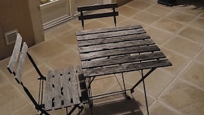 Eine Terrasse mit einem Holztisch und Stühlen, einem Blumentopf und Blick in einen Küchenbereich.