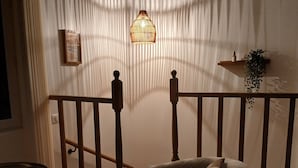 Ein gemütliches Zimmer mit Holzstuhl, kleinem Tisch, Pendelleuchte und einer Pflanze auf einem Regal.