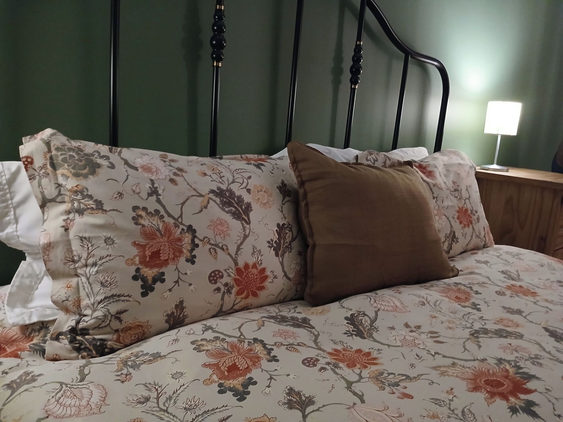 A bed with floral bedding and a brown pillow, a black metal headboard, and a nightstand with a lamp.
