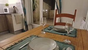 Ein Esstisch ist gedeckt mit Tellern, Besteck und Weingläsern, mit Blick auf eine Küche und eine Glastür, die zu einem Außenbereich führt.