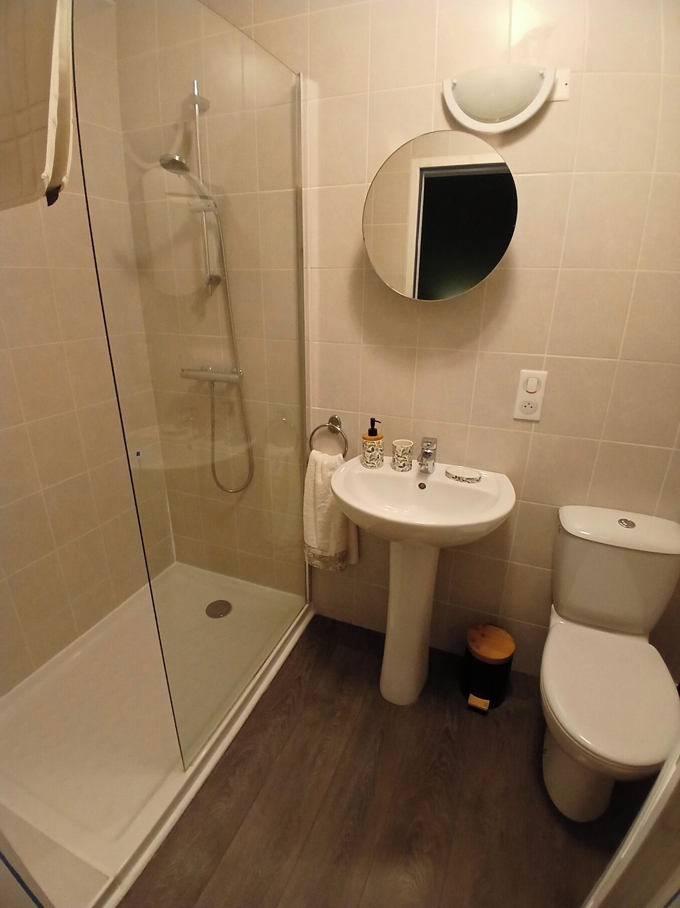 Un baño con ducha envuelta en vidrio, lavamanos pedestal, inodoro y espejo sobre el lavamanos.