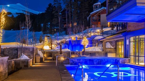 Ein Hotel mit Poolbereich, Steinmauern und Blick auf einen verschneiten Berg.