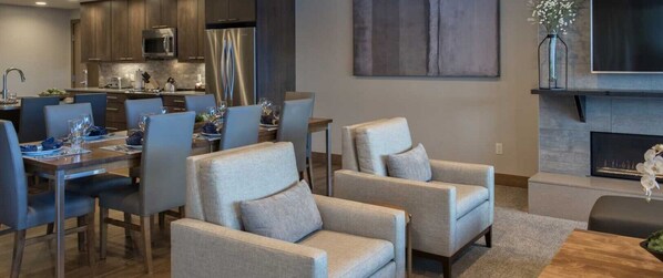 Un salon moderne avec une cheminée, des sièges confortables et un coin repas, avec une cuisine en arrière-plan.