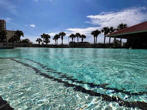A clear swimming pool with a view of palm trees and a building in the background. - Barefoot Villa: Pools, Golf, Beach, Snowbirds (North Myrtle Beach)