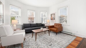 A modern living room with a grey sofa, a white armchair, a wooden coffee table, and a patterned rug. - Fox Point 3BR - Near Brown, RISD & Downtown (Providence)