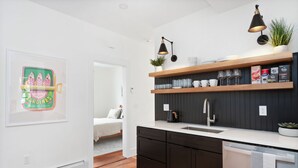 A modern kitchen with dark cabinetry, white countertops, and wooden shelves. There is a sink, a coffee maker, and a potted plant on the counter. - Fox Point 3BR - Near Brown, RISD & Downtown (Providence)