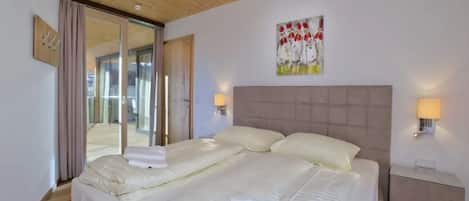 A hotel room with a double bed, a wooden ceiling, a glass door leading to a balcony, and a painting on the wall.