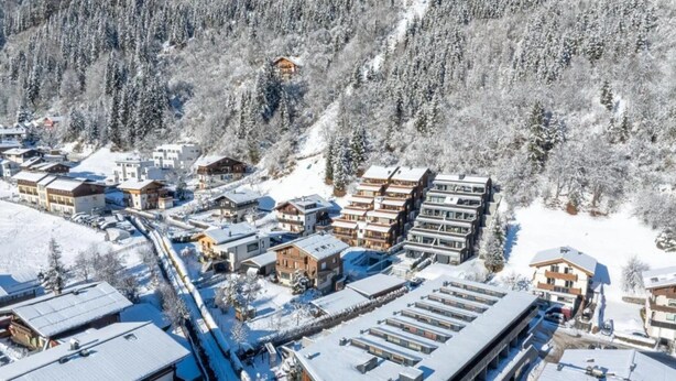 A snow-covered mountain town with modern buildings, a ski lift, and a dense forest in the background. - Top-floor Mountain Penthouse for 8 (Neukirchen am Grossvenediger)
