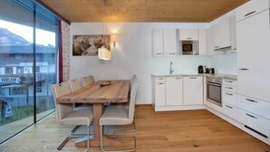 A modern kitchen with white cabinets, a wooden dining table, and a view of the outside. - Top-floor Mountain Penthouse for 8 (Neukirchen am Grossvenediger)
