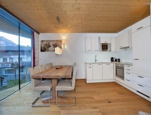 A modern kitchen with white cabinets, a wooden dining table, and a view of the outside. - Top-floor Mountain Penthouse for 8 (Neukirchen am Grossvenediger)