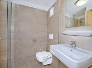Bathroom features a wall-mounted sink, mirror, and toilet, with a glass shower enclosure in the background.
