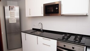A kitchen with white cabinets, a stainless steel refrigerator, a black countertop, a microwave, a sink, and a stove. - APARTMENT GRANVIA FIRA BCN🎅🏻 (Hospitalet de Llobregat)