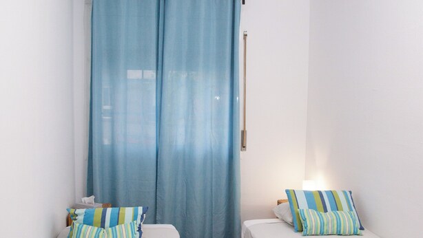 A small, clean room with two single beds, a window with blue curtains, and a ceiling light. - APARTMENT GRANVIA FIRA BCN🎅🏻 (Hospitalet de Llobregat)