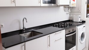 A modern kitchen with white cabinets, a black countertop, stainless steel appliances, and a built-in washing machine. - APARTMENT GRANVIA FIRA BCN🎅🏻 (Hospitalet de Llobregat)