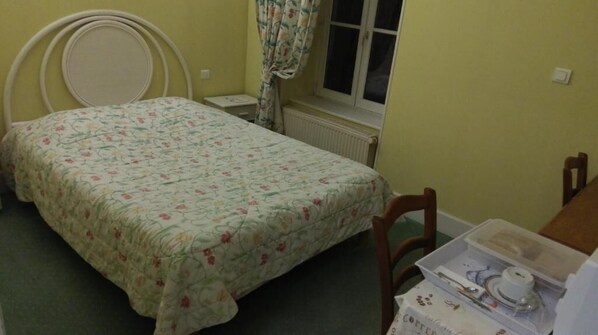 A bedroom with a bed, a nightstand, a chair, and a window with curtains. - Hôtel de l'Europe (Corbigny)