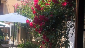 An outdoor patio with tables and chairs, surrounded by a garden with red flowers and a building in the background. - Hôtel de l'Europe (Corbigny)