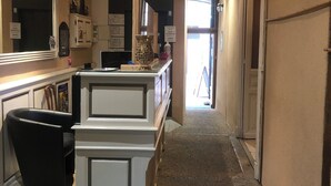 A hotel lobby with a reception desk, a black chair, a white counter, and a door leading to another room. - Hôtel de l'Europe (Corbigny)