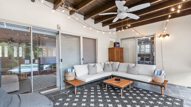 A modern outdoor living area with a white sectional sofa, wooden coffee table, and a ceiling fan.