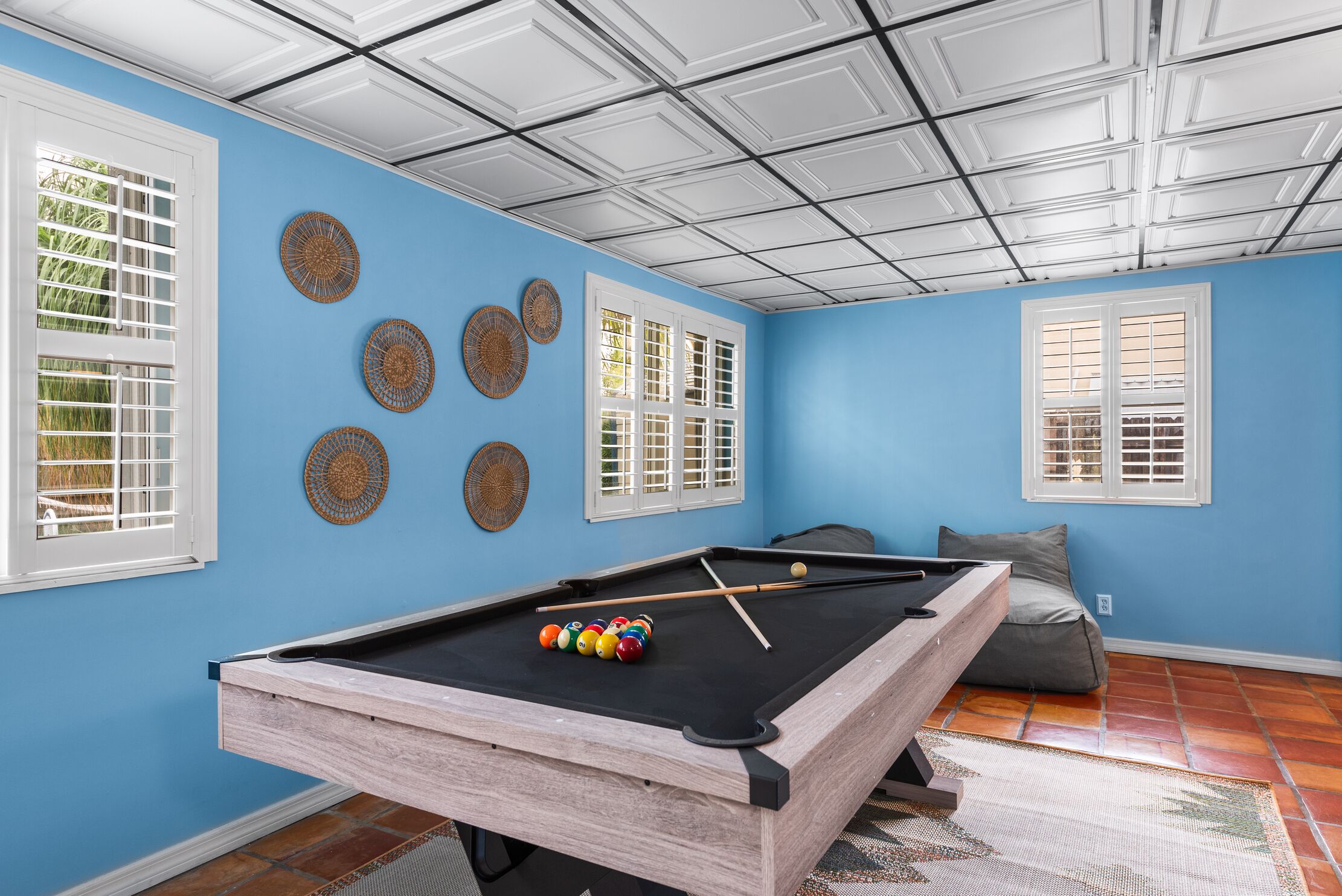 A pool table in a room with blue walls, white windows, and a ceiling with a grid pattern.