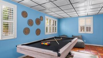 A pool table in a room with blue walls, white windows, and a ceiling with a grid pattern.