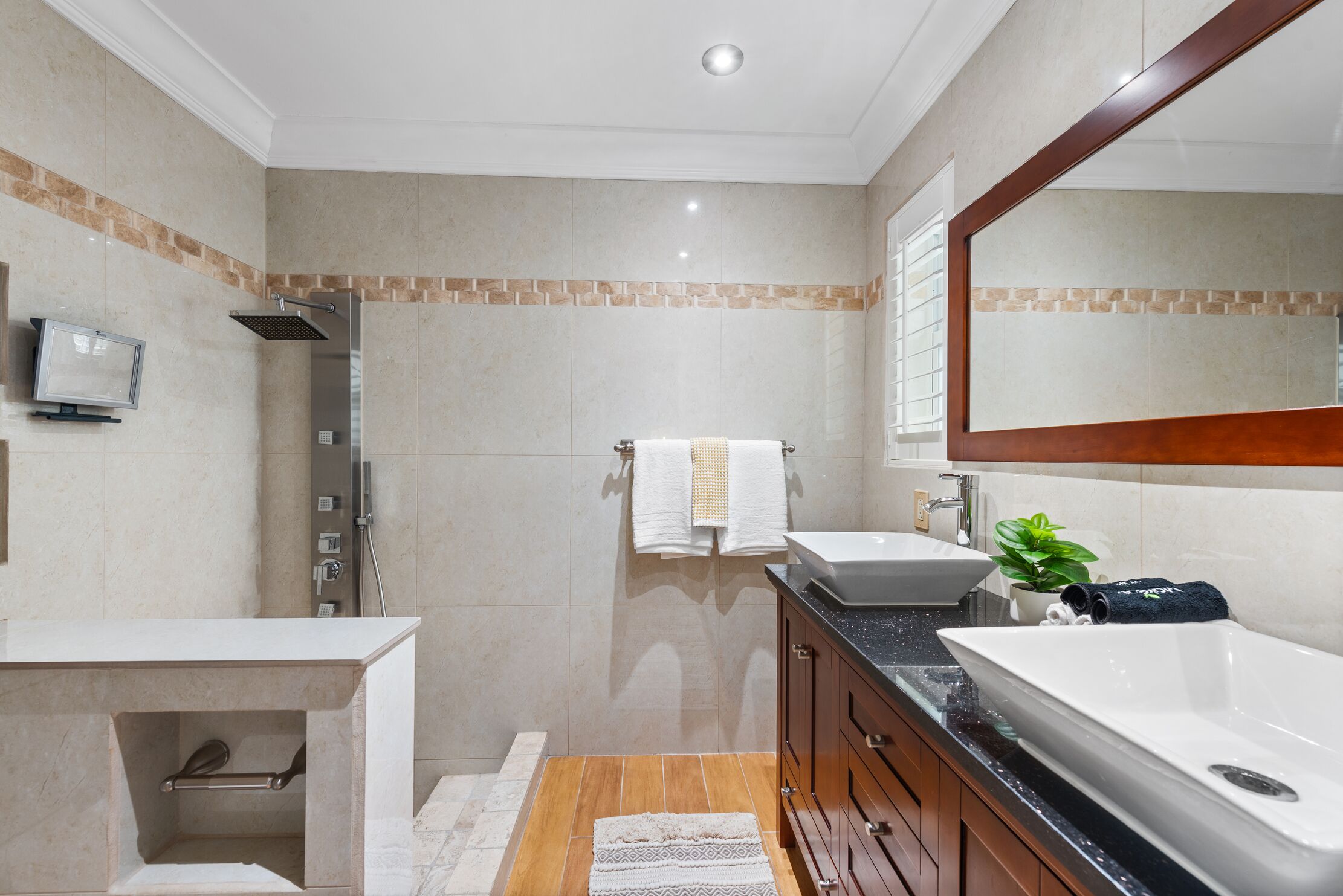 A modern bathroom with a shower, two sinks, a mirror, and a small plant.
