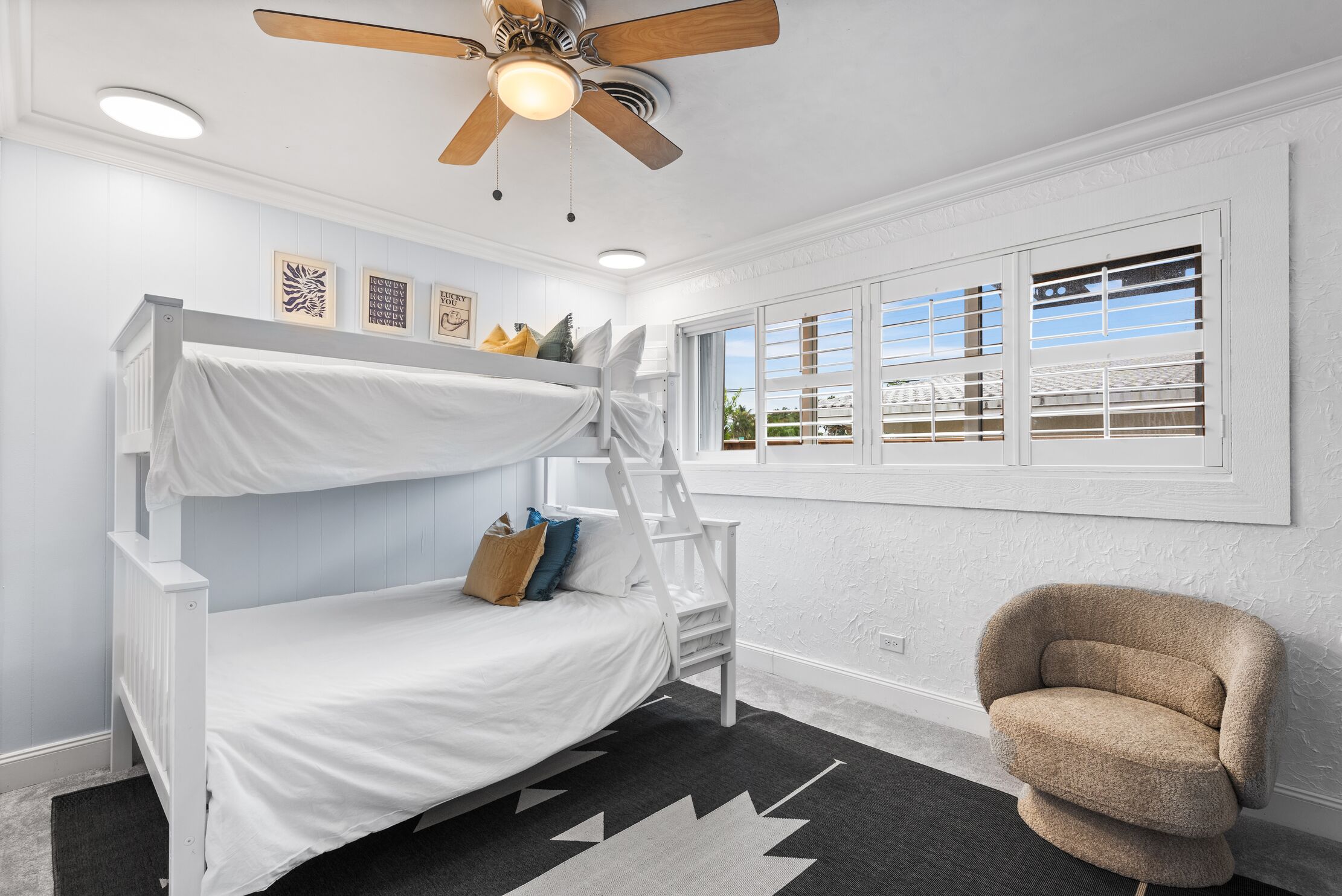 A bunk bed room with a ceiling fan, a window with blinds, and a chair.