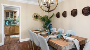 A dining area with a wooden table set for four, surrounded by chairs. A chandelier hangs above, and decorative plates are mounted on the wall.