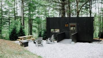 Una cabaña con una terraza de madera, sillas Adirondack y un banco.