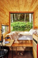 Una habitación de cabaña de madera con una cama, un escritorio y una ventana con vistas a un bosque.