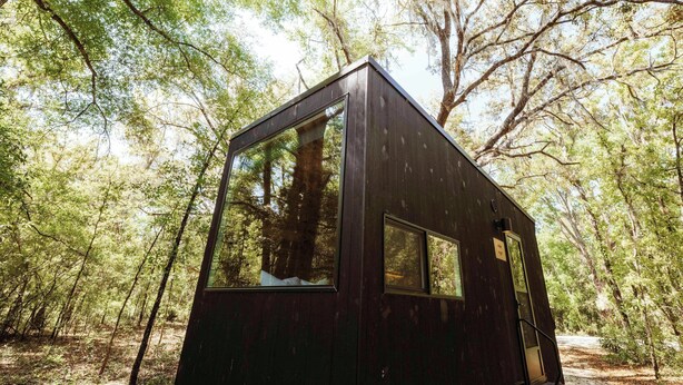 A small, dark-colored cabin with large windows, surrounded by a forest. - Postcard Cabins Big Bear, Outdoor Collection by Marriott Bonvoy (Running Springs)