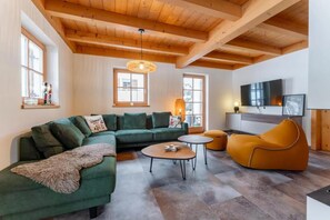 A modern living room with a green sectional sofa, a yellow bean bag, a coffee table, and a television mounted on the wall.